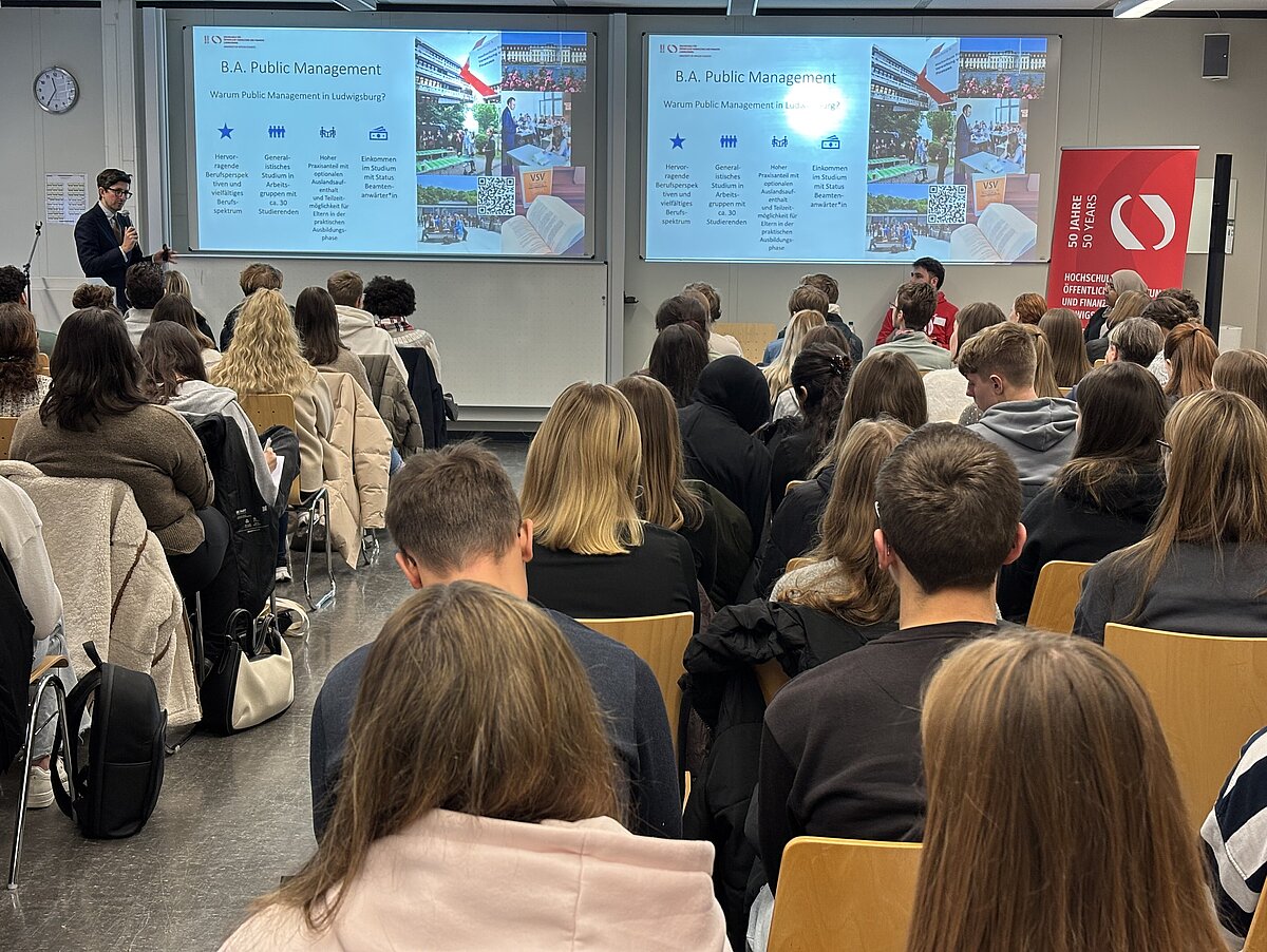 Dozent stellt den Studiengang Public Management (PM) vor vollem Hörsaal der HVF am Studieninfotag 2025 vor.