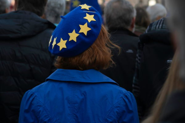 Master Europäisches Verwaltungsmanagement studieren Frau mit blauem EU-Barett in einer Menschenmenge bei einer pro-europäischen Demonstration auf dem Trafalgar Square in London, im Hintergrund sind Gebäude und eine EU-Flagge sichtbar.